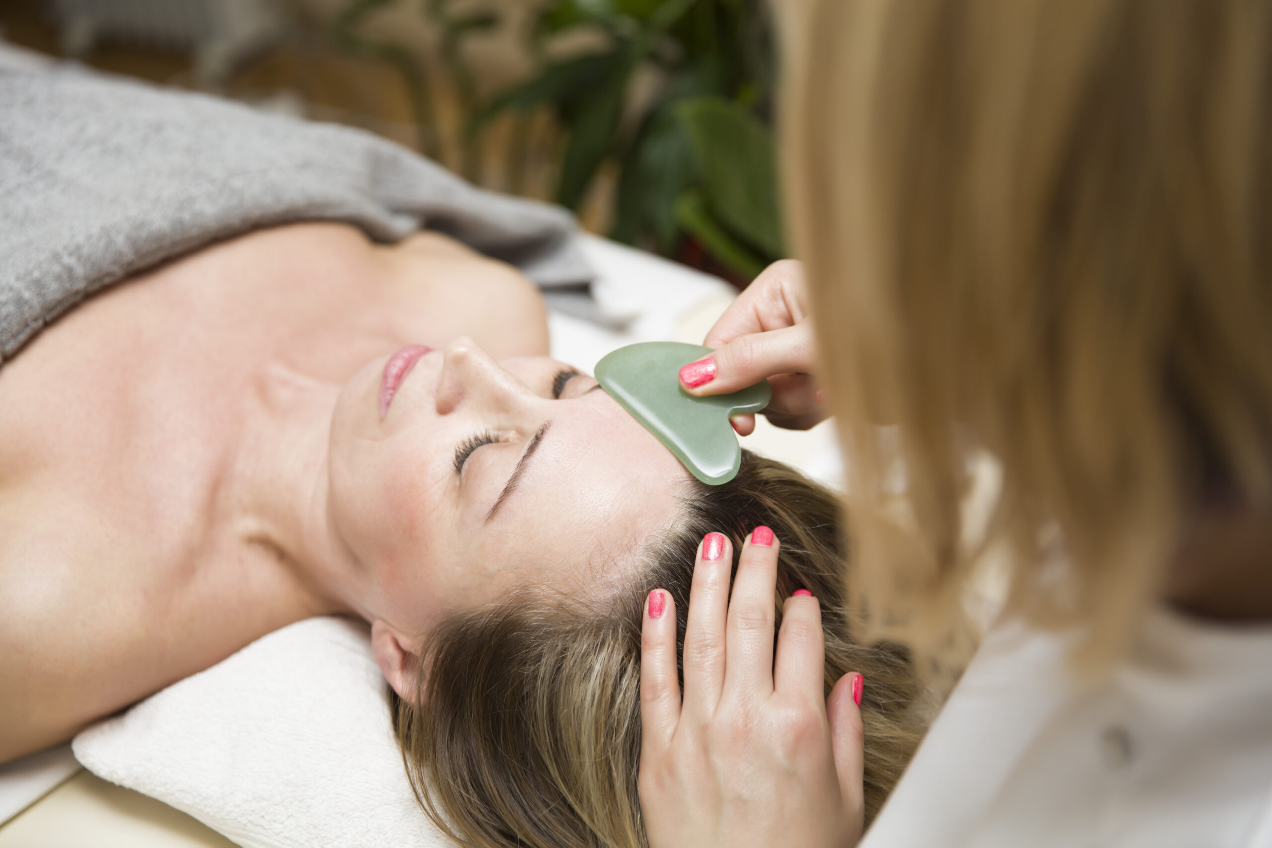 Woman having an gua sha facial massage with natural jade stone massager in the salon