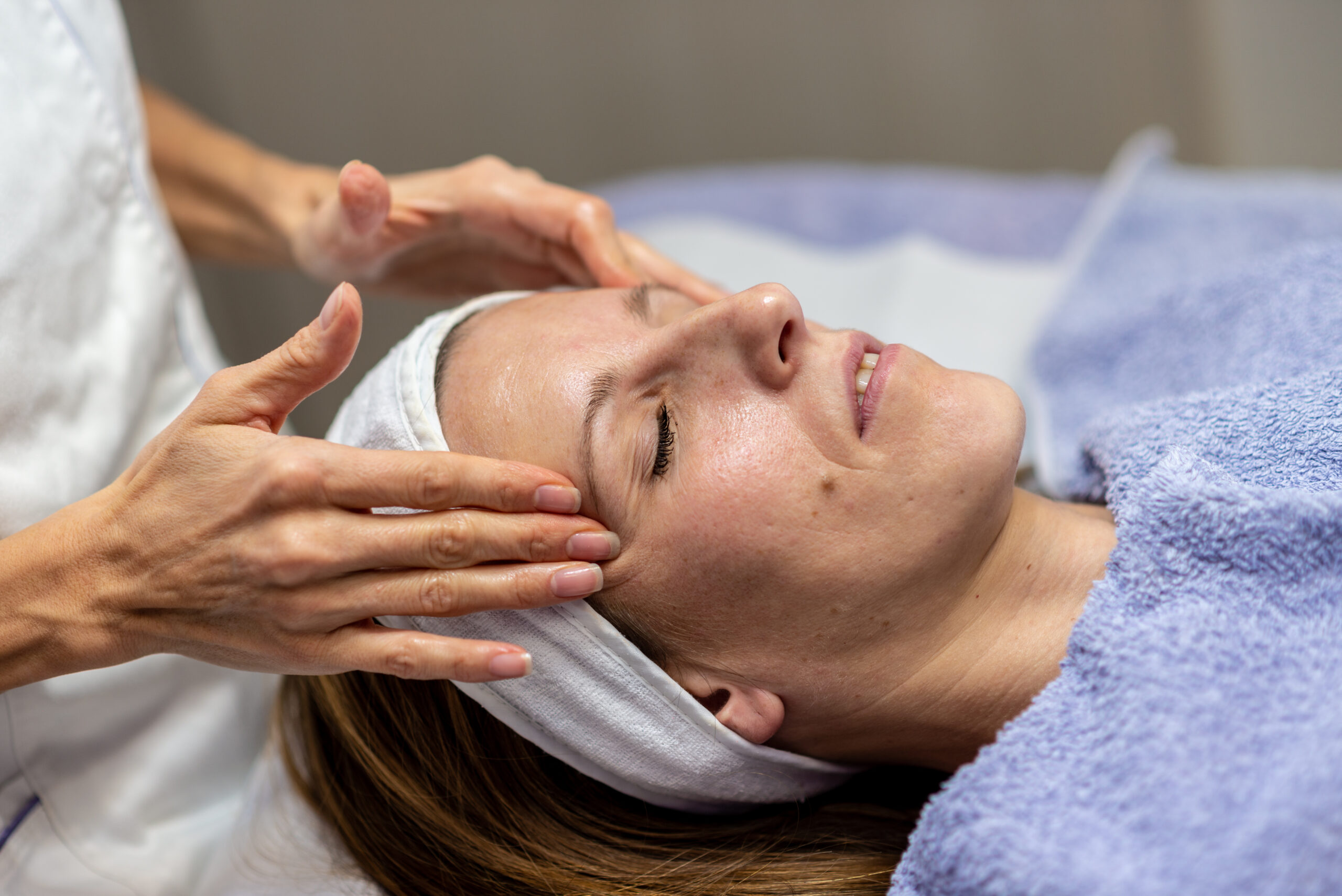 Young brunette enjoying cleansing facial massage treatment with her eyes closed lying on a table.